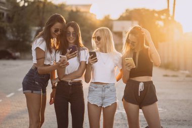 Dört çekici kadın akıllı telefonlarıyla araba parkında duruyorlar.