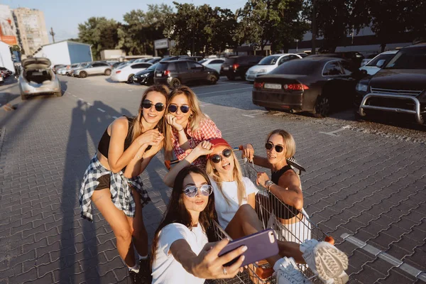 Cinco chicas jóvenes se divierten con un carrito de supermercado en un aparcamiento — Foto de Stock