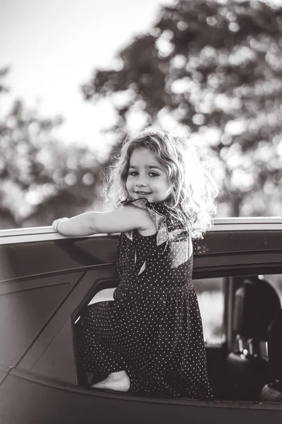 Une petite fille est debout sur la porte de la voiture — Photo