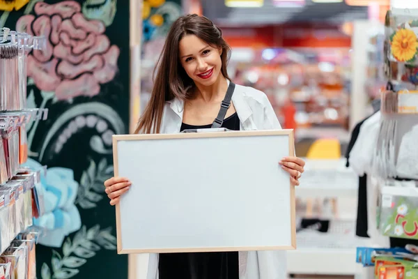 Usmívající se bruneta žena drží bílou prázdnou desku — Stock fotografie