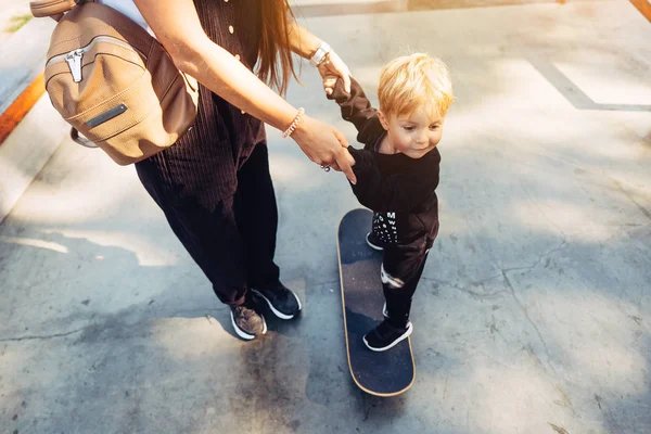 Молодая мама учит своего маленького мальчика кататься на скейтборде — стоковое фото