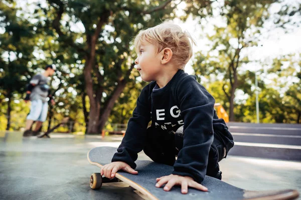 Jeune enfant assis dans le parc sur une planche à roulettes . — Photo