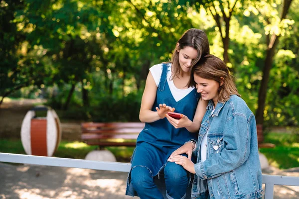 Duas namoradas femininas olham para o smartphone na embalagem — Fotografia de Stock