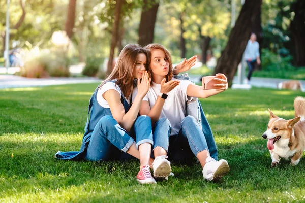 Duas amigas sentadas no parque descansam e tiram uma selfie. — Fotografia de Stock