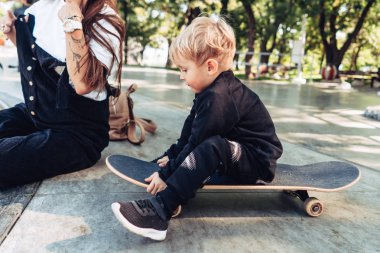 Genç anne küçük oğluna kaykay sürmeyi öğretiyor.