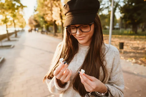 Menina bonita segurando fones de ouvido sem fio no parque — Fotografia de Stock