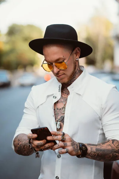 A young man in a hat and sunglasses holds a mobile phone in his hands — Stock Photo, Image