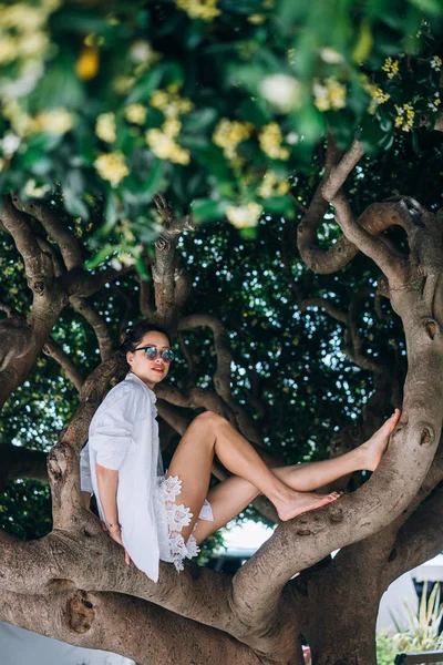 Uma bela mulher sentada numa árvore. Hora da Primavera — Fotografia de Stock