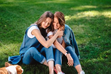 İki arkadaş parkta yeşil çimlerin üstünde oturuyor.