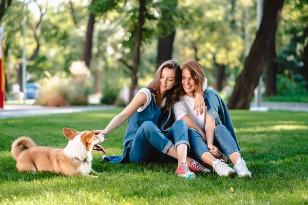 Två kvinnliga vänner i parken leker med liten hund — Stockfoto