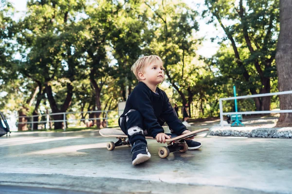 Jeune enfant assis dans le parc sur une planche à roulettes . — Photo