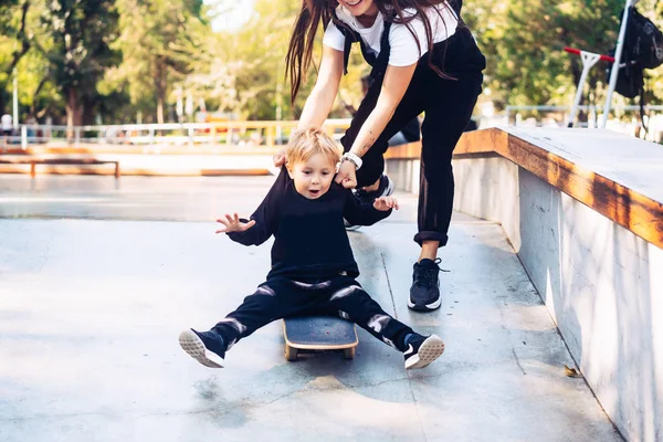 Joven madre enseña a su pequeño niño a montar un monopatín — Foto de Stock