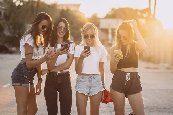 Τέσσερις ελκυστικές γυναίκες στέκονται στο χώρο στάθμευσης αυτοκινήτων με smartphones — Φωτογραφία Αρχείου