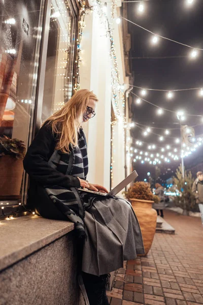 Tampilan samping wanita muda menggunakan laptop di jalan dengan kota malam — Stok Foto