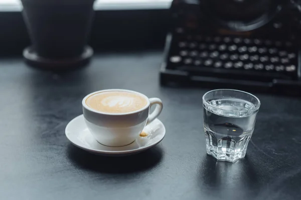 A cup of cafe latte coffee in a ceramic cup and a glass of water — Stock Photo, Image