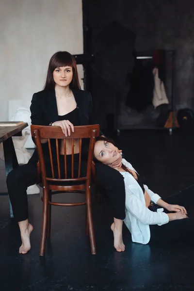 两个女孩摆姿势拍照, 一个坐在椅子上, 另一个坐在地板上 — 图库照片