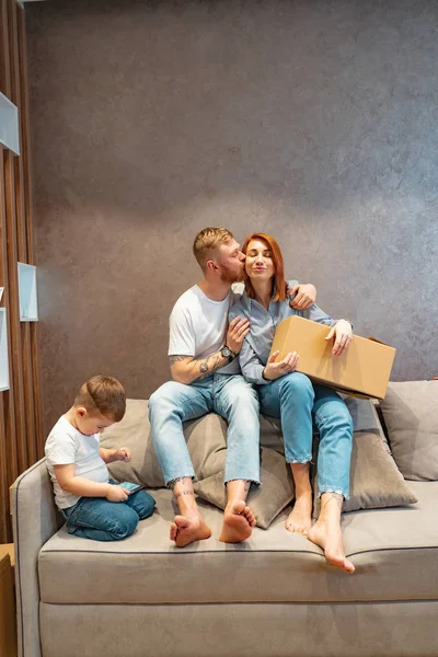 Νέοι ευτυχισμένη οικογένεια με παιδί αποσυσκευασία καθιστή μαζί κουτιά, στον καναπέ — Φωτογραφία Αρχείου