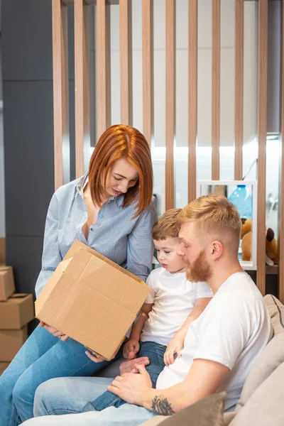 Joven familia feliz con niños desempacando cajas juntos sentados en el sofá — Foto de Stock