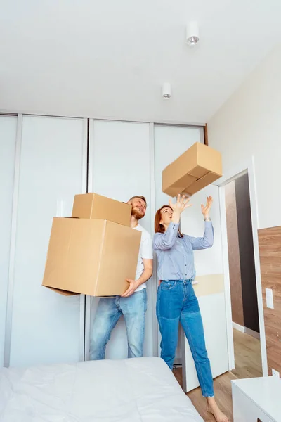 Pareja feliz sosteniendo cajas de cartón y mudándose a un nuevo lugar — Foto de Stock