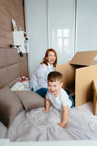 Mamá e hijo pequeño juegan en el dormitorio con cajas de papel . — Foto de Stock