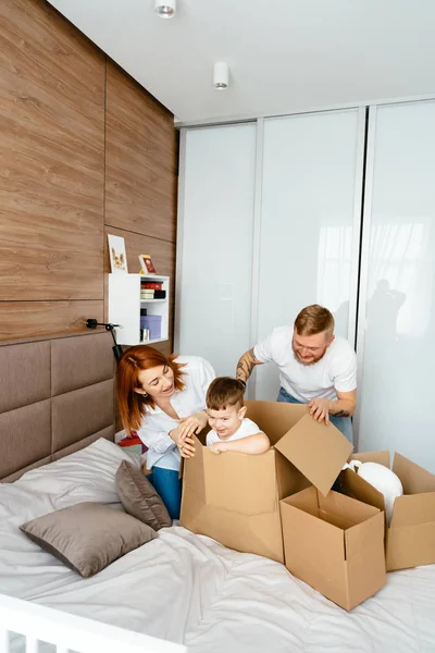 Папа мама и маленький сын играют в спальне с бумажными коробками — стоковое фото
