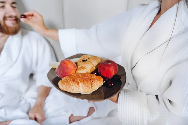 O cara e a menina roupão de banho, menina alimenta a fruta cara — Fotografia de Stock