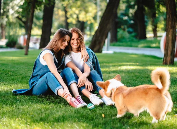 Två kvinnliga vänner i parken leker med liten hund — Stockfoto