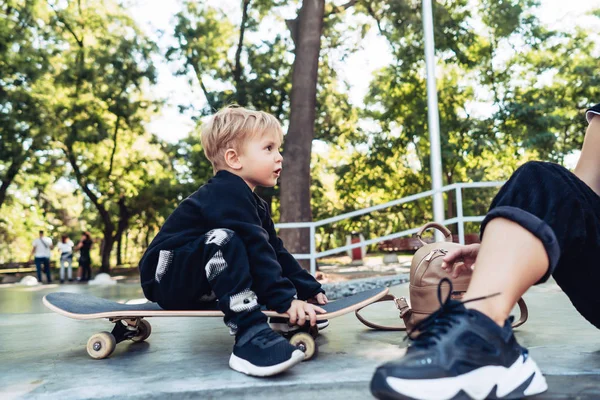Jeune enfant assis dans le parc sur une planche à roulettes . — Photo