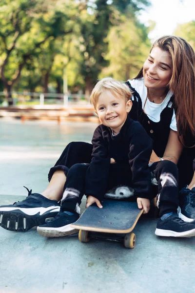 Молодая мама учит своего маленького мальчика кататься на скейтборде — стоковое фото