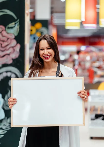 Mujer morena sonriente sosteniendo tablero blanco en blanco —  Fotos de Stock