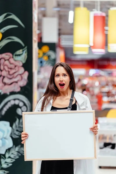 Usmívající se bruneta žena drží bílou prázdnou desku — Stock fotografie