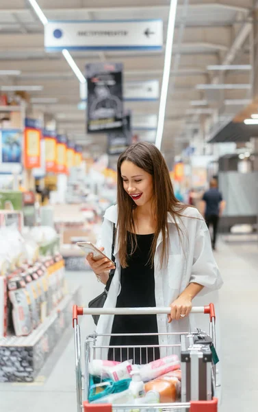 Lächelnde junge Frau mit Smartphone im Supermarkt — Stockfoto