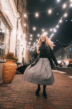 Sokakta dizüstü bilgisayarla poz veren genç bir kadın.