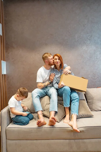 Joven familia feliz con niños desempacando cajas juntos sentados en el sofá — Foto de Stock