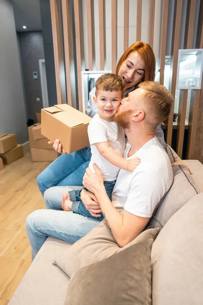 Joven familia feliz con niños desempacando cajas juntos sentados en el sofá — Foto de Stock
