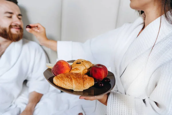 O cara e a menina roupão de banho, menina alimenta a fruta cara — Fotografia de Stock