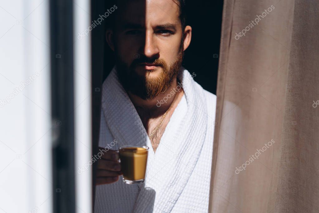Male in white bathrobe with coffee mug in hand.