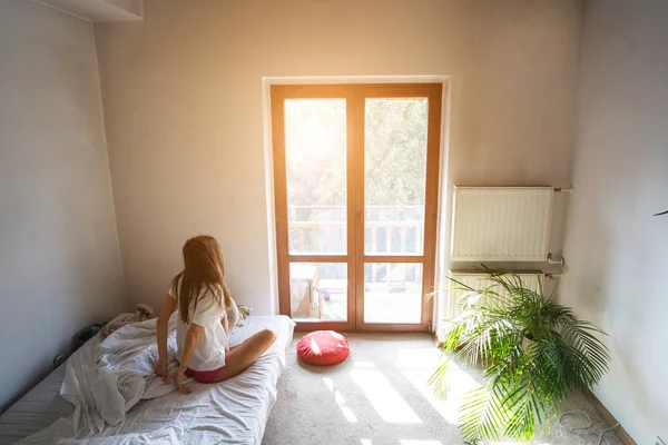 Junge Frau sitzt auf Bett und schaut aus dem Fenster. — Stockfoto