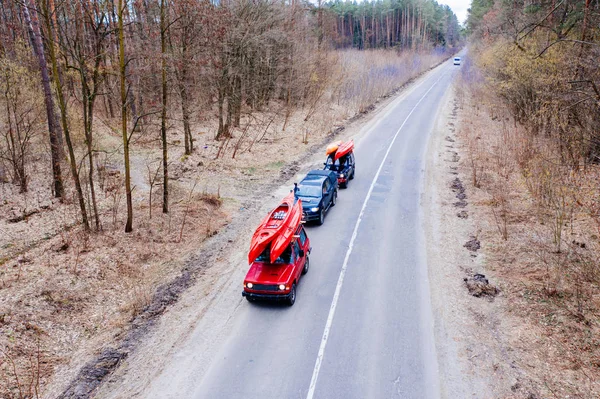 Vários carros com caiaques no telhado rack de condução na estrada entre árvores — Fotografia de Stock