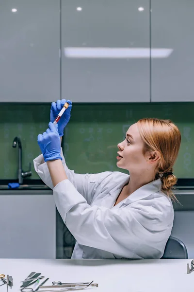 Женщина-медицинский или научный исследователь смотрит на пробирку в лаборатории . — стоковое фото