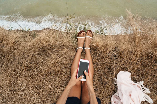 Bela jovem sentada e segurando um smartphone em suas mãos, vista superior — Fotografia de Stock