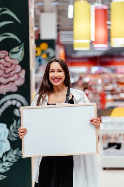 Gülen esmer kadın elinde beyaz bir tahta tutuyor.