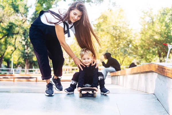 Jeune mère enseigne à son petit garçon à monter sur un skateboard — Photo