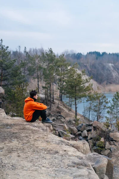 En ung mand sidder på kanten af en klippe udgør for kameraet - Stock-foto