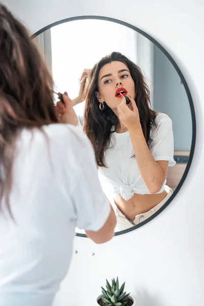 Young woman applying lipstick looking at mirror — Stock Photo, Image