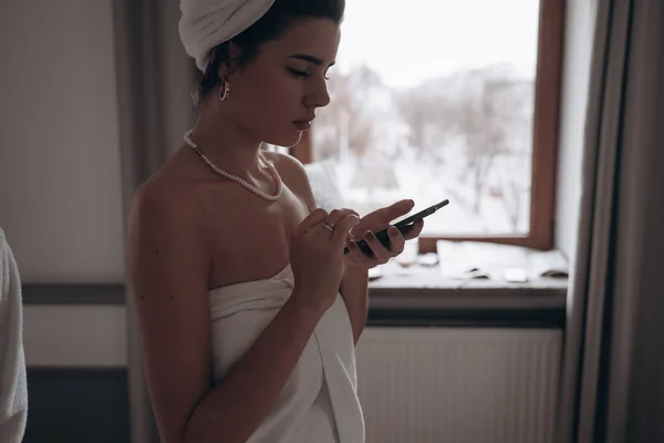 Красотка в халате и с полотенцем на голове с помощью смартфона — стоковое фото