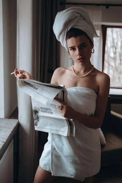 Hermosa joven en una toalla fuma un cigarrillo y lee el periódico — Foto de Stock