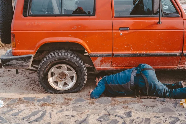 Homem encontra-se sob um carro 4x4 em uma estrada de terra — Fotografia de Stock