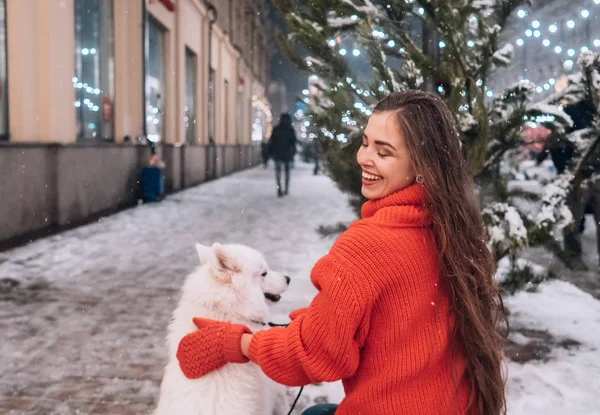 A young woman crouched beside a dog on a winter street.