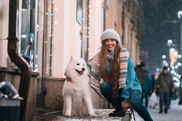 A young woman crouched beside a dog on a winter street.